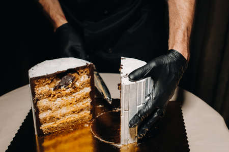 Amazing Cakes. A black-gloved chef is slicing a chocolate wedding cake. The wedding Cake is delicious inside on a black background.Large cake in white chocolateの写真素材