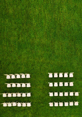 Top view of White wooden chairs standing in rows on a green field waiting for guests.View from a...
