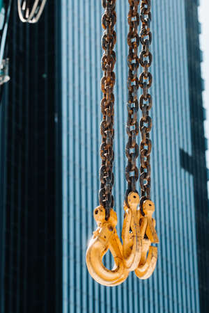 The hooks of the mobile crane near the glass of high buildings.Lots of hooks hanging from chains suspended from a craneの写真素材
