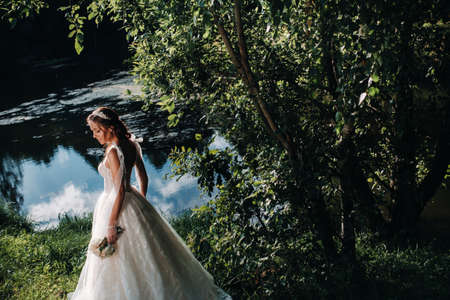 portrait of an elegant bride in a white dress with a bouquet in nature in a nature Park.Model in a wedding dress and gloves and with a bouquet .Belarusの写真素材