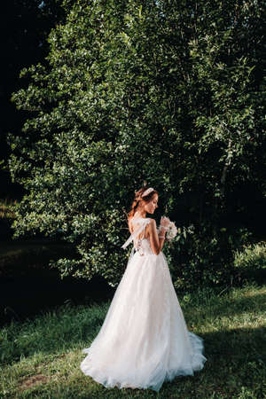 portrait of an elegant bride in a white dress with a bouquet in nature in a nature Park.Model in a wedding dress and gloves and with a bouquet .Belarusの写真素材