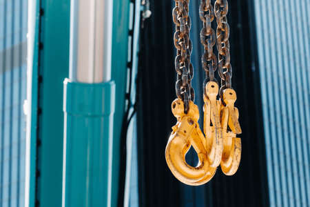 The hooks of the mobile crane near the glass of high buildings.Lots of hooks hanging from chains suspended from a craneの素材 [FY310152873515]