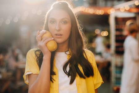 a girl in a yellow shirt with lemons in her hands on a city street. Portrait of a woman in yellowの写真素材