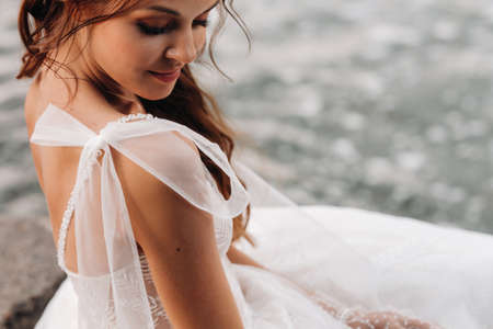 An elegant bride in a white dress and gloves is sitting by the lake in the Park, enjoying nature.A model in a wedding dress and gloves in a nature Park.Belarusの写真素材