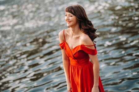 a young beautiful girl with long brown hair, in a long red dress with a ring around the lake.の写真素材
