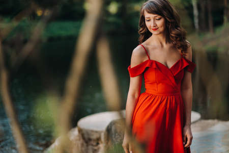 a young beautiful girl with long brown hair, in a long red dress with a ring around the lake.の写真素材