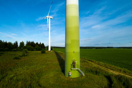 A man in a business suit with a green Golf shirt stands next to a windmill against the background of...