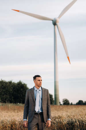Portrait of a businessman in a gray suit on a wheat field against the background of a windmill and...