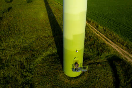 A man in a business suit with a green Golf shirt stands next to a windmill against the background of...