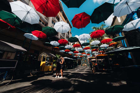 Port Louis, Mauritius, a black-clad couple stands on an umbrella-covered city alley leading to the capital.の写真素材