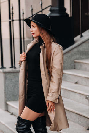 Stylish young woman in a beige coat in a black hat on a city street. Women's street fashion. Autumn clothing.Urban style.の写真素材