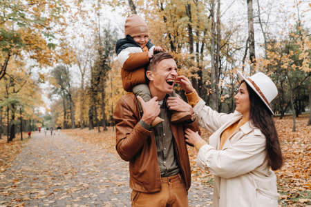Father and mother with son walking in the autumn Park. A family walks in the Golden autumn in a nature Park.の写真素材