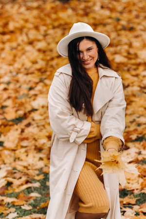 a cheerful girl in a white coat and hat smiles in an autumn Park.portrait of a smiling woman in Golden autumn.の写真素材