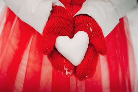 hands in red mittens close-up holding a heart made of snow.A heart made of snowの写真素材