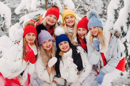 A large group of girls with lollipops in their hands stands in the winter forest.Girls in red and white clothes with candy in a snow-covered forestの写真素材