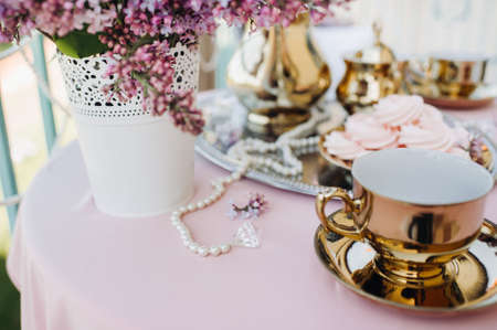 Delicate morning tea table setting with lilac flowers, antique spoons and dishes on a table with a pink tablecloth.の写真素材