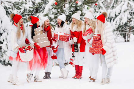 A large group of girls with Christmas gifts in their hands standing in the winter forest.Girls in red and white clothes with Christmas gifts in the snowy forest.の写真素材