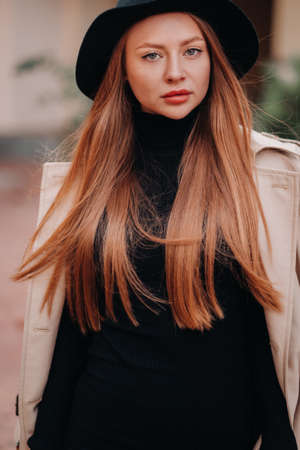 Stylish young woman in a beige coat in a black hat on a city street. Women's street fashion. Autumn clothing.Urban style.の写真素材