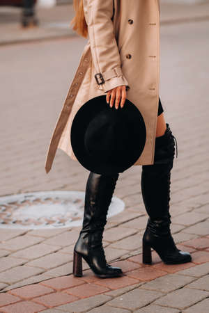 Stylish young woman in a beige coat and a black hat in his hands and glasses on a city street....