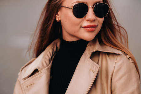 Stylish young woman in a beige coat and glasses on a city street. Women's street fashion. Autumn clothing.Urban styleの写真素材