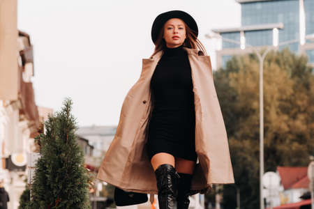 Stylish young woman in a beige coat in a black hat on a city street. Women's street fashion. Autumn clothing.Urban style.の写真素材