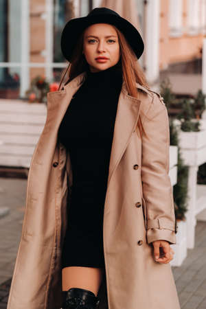 Stylish young woman in a beige coat in a black hat on a city street. Women's street fashion. Autumn clothing.Urban style.の写真素材