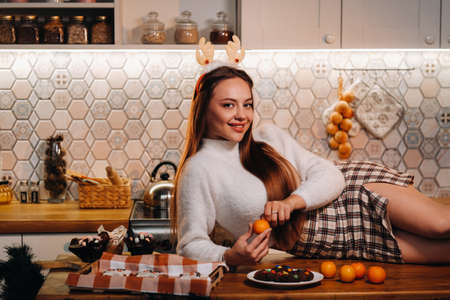A girl at Christmas is lying on the kitchen table and holding a tangerine in her hands.Woman on new year's eve in the kitchen lying with horns.の写真素材