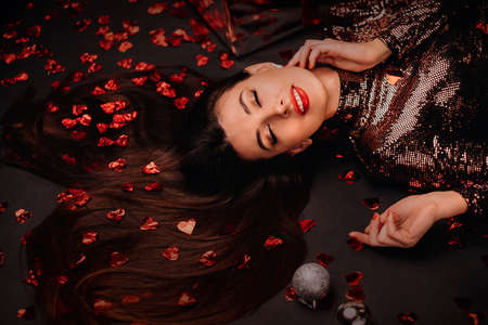 Top view of a girl in a shiny dress on the floor in confetti in the form of hearts and gifts.の写真素材