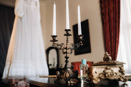 Vintage wedding dress hanging on a wooden hanger and a candle holder standing on a table in the castle.の写真素材