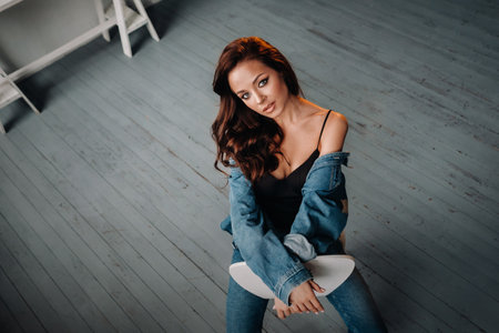 a brunette girl with long hair poses in a studio sitting on a chair