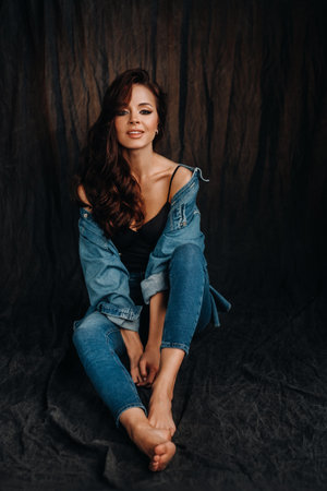 a brunette with long hair poses in a studio sitting on the floor on a black background.の写真素材