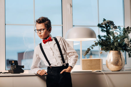 A boy in a shirt with a red bow tie and glasses stands at the window.の写真素材