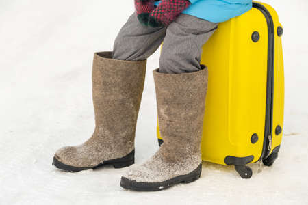A girl in winter in felt boots sits on a suitcase on a frosty snowy day