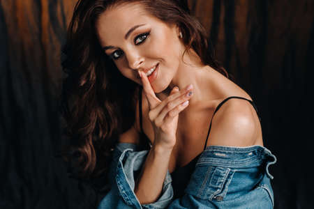 a brunette with long hair poses in a studio sitting on the floor on a black backgroundの写真素材
