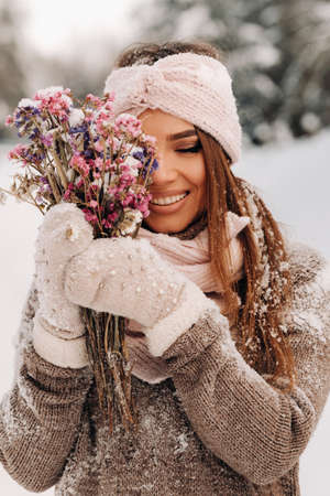 A girl in a sweater in winter with a bouquet in her hands stands among large snowdriftsの写真素材