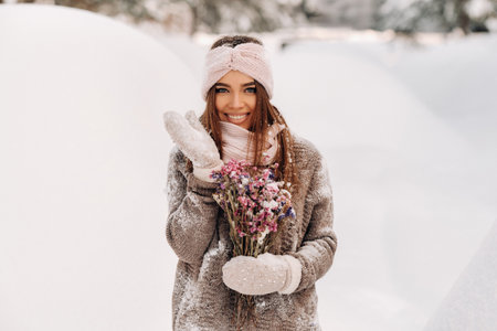 A girl in a sweater in winter with a bouquet in her hands stands among large snowdriftsの写真素材