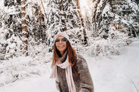 A girl in a sweater and glasses walks in the snow-covered forest in winterの写真素材