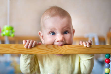 Closeup portrait of lonely toddler bites wooden bed frame. Child concept
