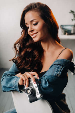 a brunette with long hair poses in a studio sitting on a chair with a camera in her hands.の写真素材