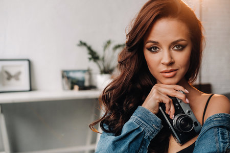 a brunette with long hair poses in a studio sitting on a chair with a camera in her hands.の写真素材