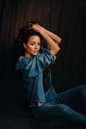 a brunette with long hair poses in a studio sitting on the floor on a black backgroundの写真素材