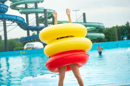 a woman in a swimsuit with rubber inflatable circles plays and has a good time near the pool of the summer water parkの写真素材