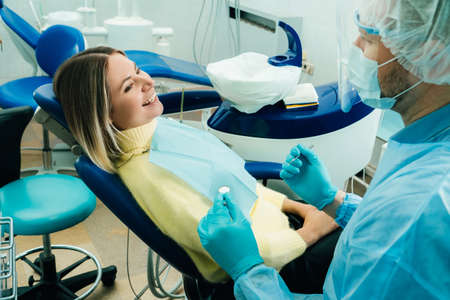 a dentist wearing a protective mask sits nearby and holds instruments in his hands before treating a...