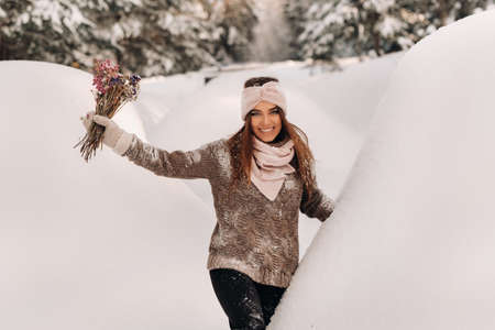 A girl in a sweater in winter with a bouquet in her hands stands among large snowdriftsの写真素材