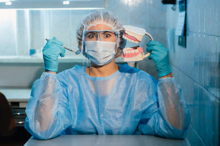 A dental doctor wearing blue gloves and a mask holds a dental model of the upper and lower jaws and a dental mirror.の写真素材