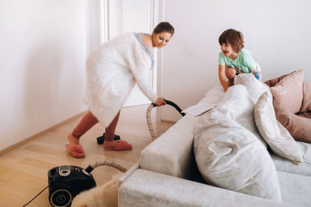 the mother vacuums the floor at home and the son watches and laughs at it.の写真素材