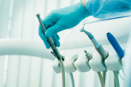 a dentist wearing gloves in the dental office holds a tool before working.