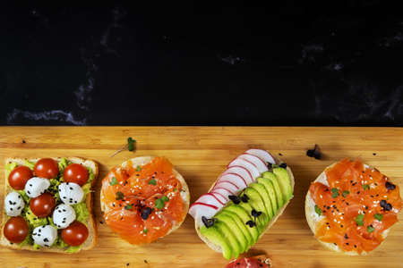 Assorted sandwiches with fish, cheese, meat and vegetables lying on the board.