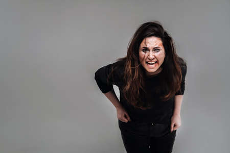 a battered woman in black clothes on an isolated gray background. Violence against women.の写真素材