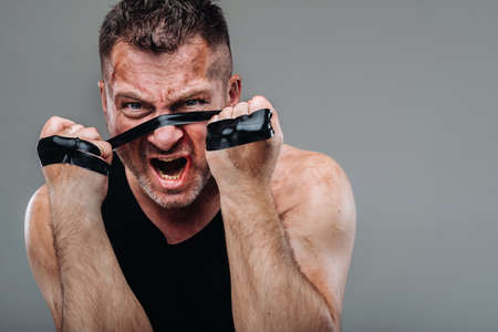 on a gray background stands a battered man in a black T shirt looking like a fighter and preparing...